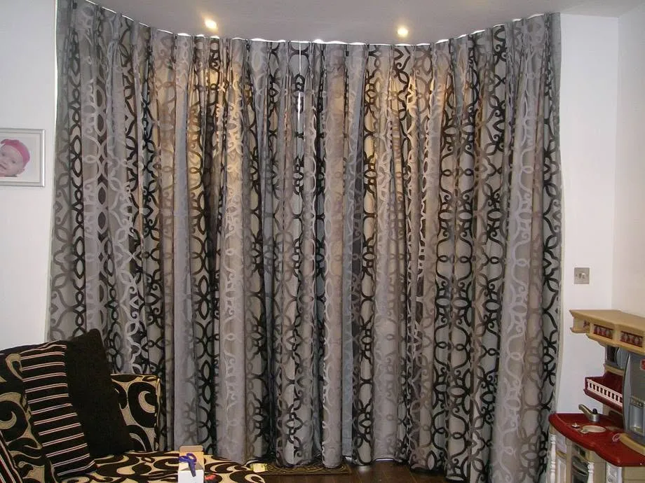 Grey pinch-pleat curtains framing a bay window beside a lamp