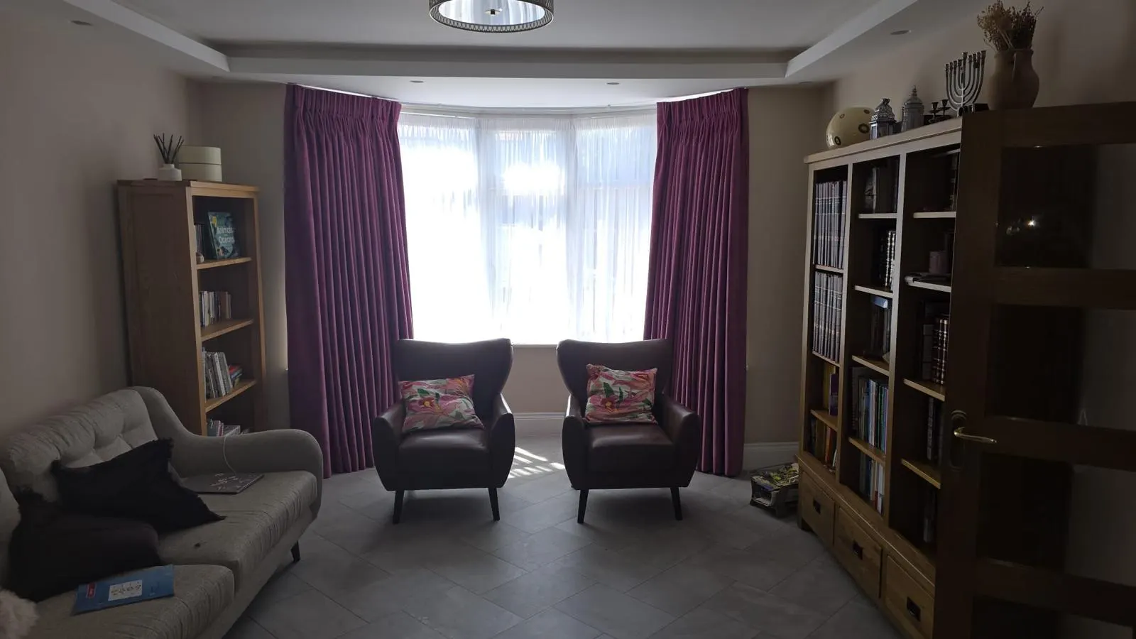 Plum pinch-pleat curtains and white sheers dressing a wide bay window in daylight