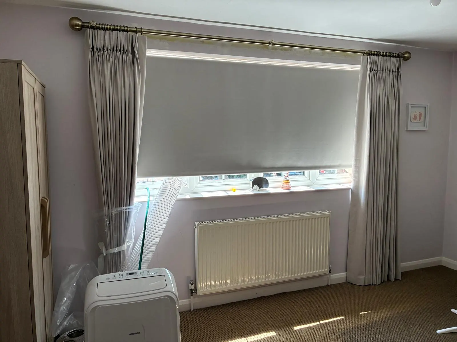 Blackout roller blind paired with pinch-pleat curtains on a brass pole