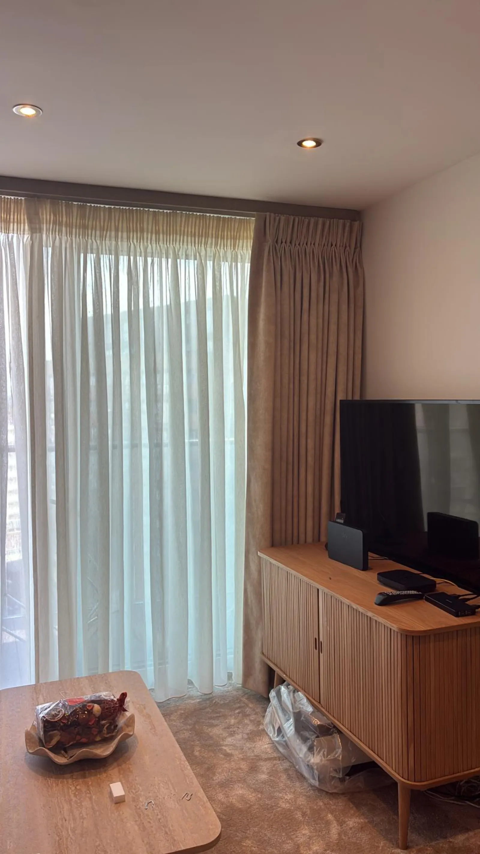Taupe pinch-pleat curtains layered over sheers beside a TV corner