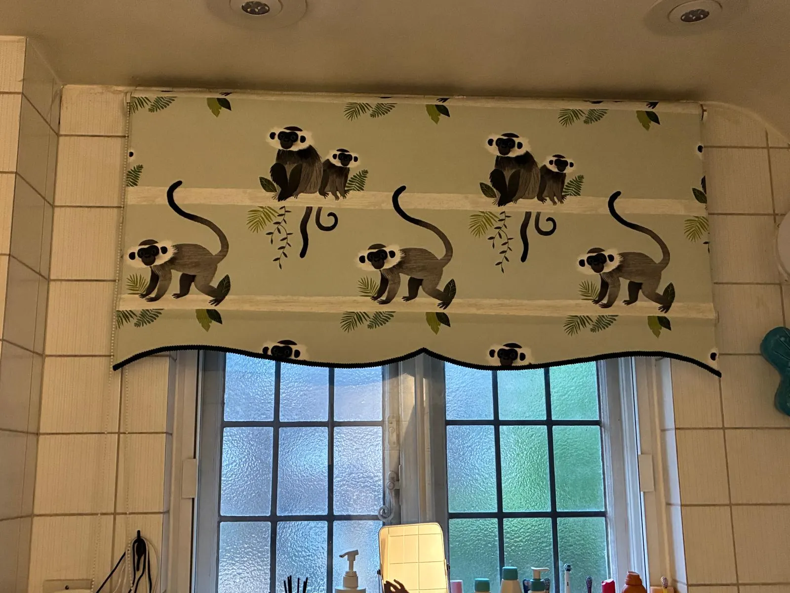Patterned roller blind finished with a scalloped, trimmed valance over a bathroom window